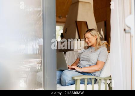 Smiling woman using laptop on sofa Stock Photo