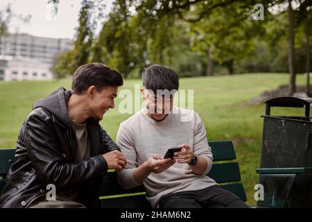 Men sitting on bench and looking at cell phone Stock Photo