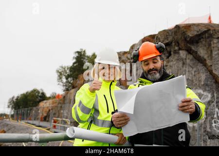 Engineers in reflecting clothing looking at blueprints Stock Photo