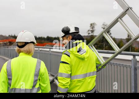 Engineers in reflective clothing carrying ladder Stock Photo