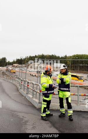 Male engineers in reflecting clothing talking at building site Stock Photo