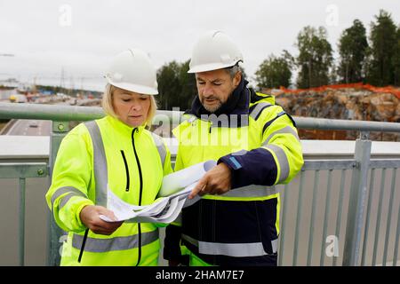 Engineers in reflecting clothing looking at blueprints Stock Photo