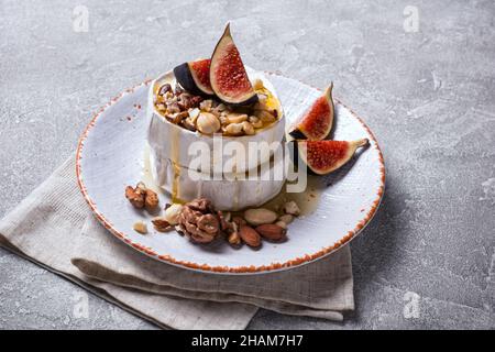 Gourmet appetizer of white brie cheese or camembert with fresh figs, nuts and honey on gray concrete background Stock Photo