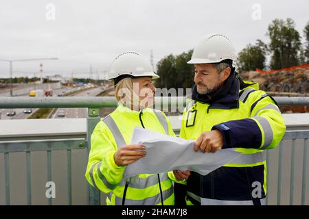 Engineers in reflecting clothing looking at blueprints Stock Photo