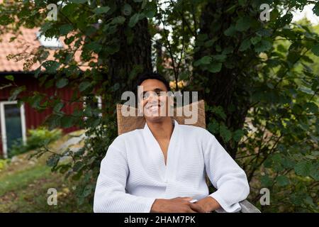 Smiling young man in bathrobe sitting outdoors Stock Photo