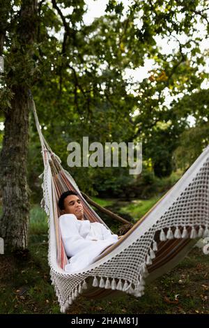 Young man in bathrobe relaxing in hammock Stock Photo