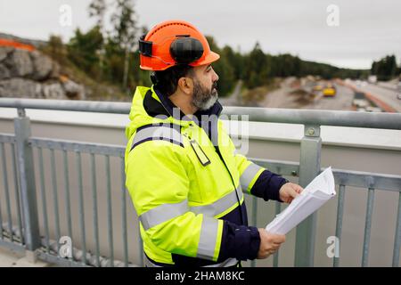 Male engineer in reflecting clothing holding blueprint Stock Photo