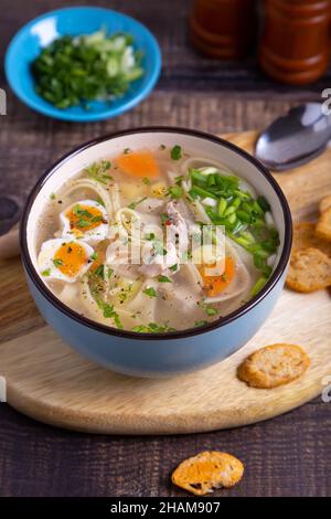 Soup with chicken, noodles, potatoes, quail eggs and carrots. Seasoned with onions and parsley. Close-up. Stock Photo