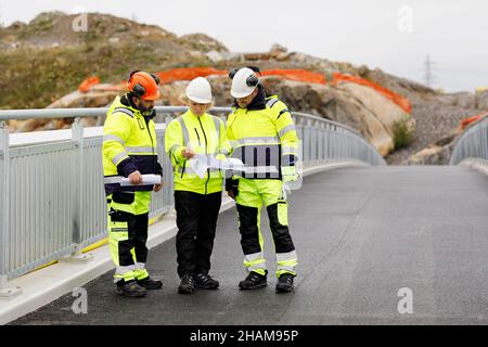 Engineers in reflective clothing looking at plans on bridge Stock Photo