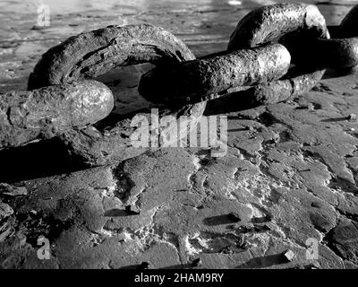 Black and white photograph of thick chain on concrete Stock Photo