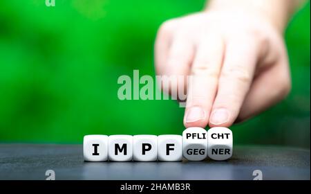 Symbol for introducing a compulsory vaccination against covid 19. Hand turns dice and changes the German expression "Impfgegner" (anti-vaxxer ) to "Im Stock Photo