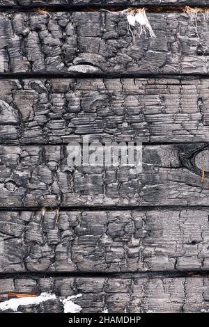 Black textured full frame backdrop of charred stack of wooden desks with snow and cracks Stock Photo