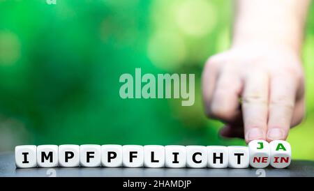 Symbol for introducing a compulsory vaccination. Hand turns dice and changes the German expression "Impfpflicht nein" (compulsory vaccination no) to " Stock Photo