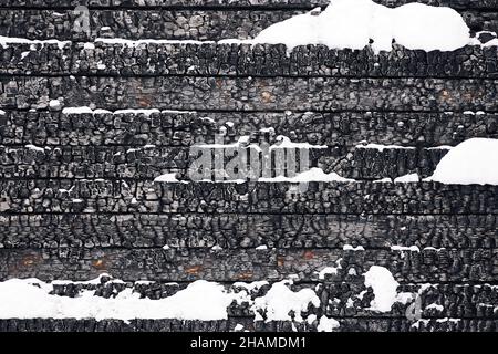 Black textured full frame backdrop of charred stack of wooden desks with snow and cracks Stock Photo