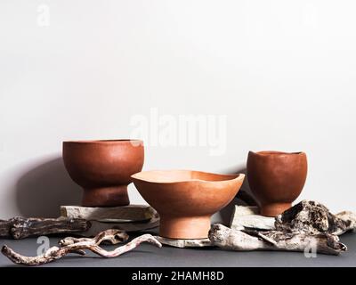 Stylish brown clay bowls on stone and driftwood on grey background. Front view. Copy spce Stock Photo