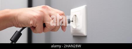 Woman hand inserts an electrical plug into outlet closeup Stock Photo