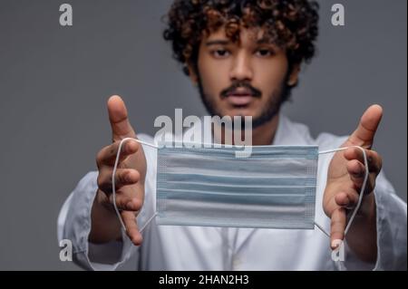 Bearded curly-haired physician holding a face covering before him Stock Photo