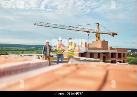 Men standing at top of unfinished house discussing Stock Photo