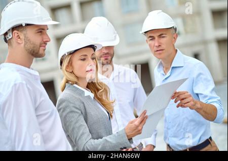 Woman with drawing listening to engineer and waiting workers Stock Photo