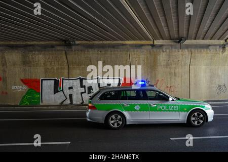 A German police car on a mission with rotating blue lights in a underpass  whose wall is covered with graffiti. Stock Photo