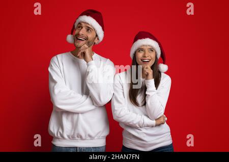 Pensive Young Couple Wearing Santa Hats Thinking About Something Over Red Background Stock Photo
