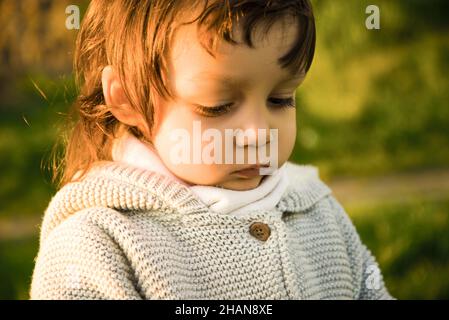 Little cute happy smiling baby boy sitting in field on fresh green grass sunny day. Stock Photo