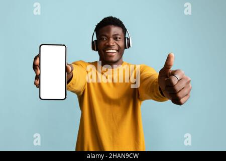 Handsome african american young man with headphones showing cellphone, mockup Stock Photo