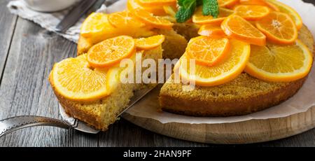 Orange polenta and almond cake decorated with candied orange and tangerines slices on old wooden background. Upside down polenta cake. Homemade cake w Stock Photo