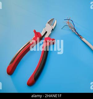 Cutting a computer network wire with wire cutters, blue studio background Stock Photo