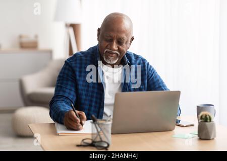 Senior Black Man At Laptop Taking Notes Indoors Stock Photo