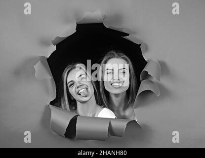 Beautiful girls peeks out of a hole in blue torn paper on a dark background. Stock Photo