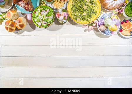 Festive dinner, Easter brunch. Traditional Easter dishes on family home table - baked meat, quiche, spring salad, muffin, colored eggs, hot cross buns Stock Photo