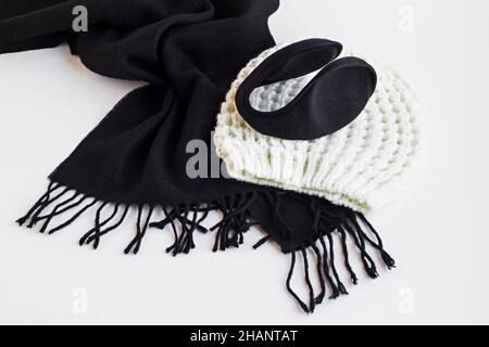 Unisex black scarf,ear flaps and white color hand-knitted beanie on the white surface.Conceptual image of winter season. Stock Photo