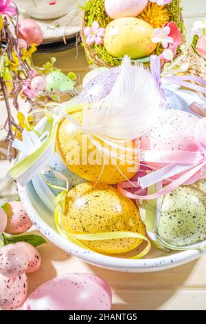 Easter painted colorful pastel eggs in a basket, with feathers on a light wood background. Easter greeting card composition, spring holiday still life Stock Photo