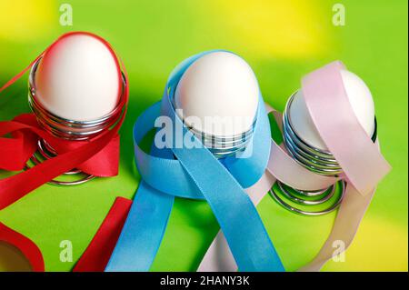 coloful Easter eggs and white eggs in silver egg stand with joyful ribbons  over jolly spring green yellow background Stock Photo