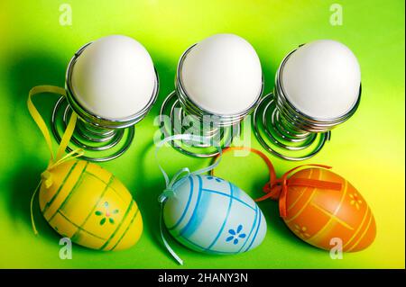 coloful Easter eggs and white eggs in silver egg stand with joyful ribbons  over jolly spring green yellow background Stock Photo