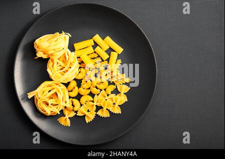 various types of pasta like fettuccine, fusilli, farfalle on a black plate Stock Photo