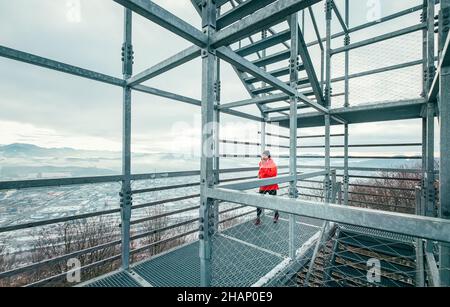 Alone runner man dressed bright red softshell waterproof sporty jacket running up by huge steel industrial tower stairs in cold winter day with pictur Stock Photo