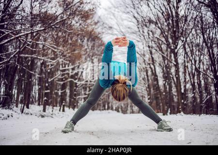 Fit sportswoman standing in snow in forest and doing fitness exercises. Healthy life, winter fitness Stock Photo