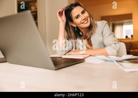 Cheerful interior designer sitting at her desk in her home office. Creative businesswoman smiling at the camera while taking a short break. Happy fema Stock Photo