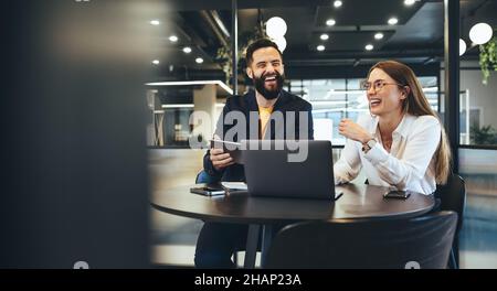 Two happy young businesspeople working together in a modern workspace. Two young entrepreneurs smiling cheerfully while working with wireless technolo Stock Photo
