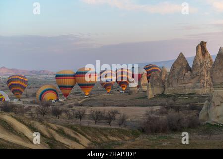 Dozens of hot-air balloons with hundreds of tourists lifting off early in the morning near Goreme, Cappadocia,  Central Anatolia, Turkey Stock Photo