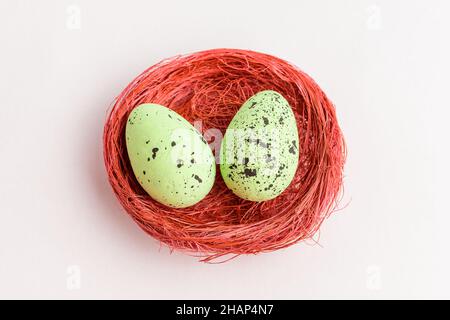 Two green colored decorative Easter eggs in a red rustic basket isolated on a white table Stock Photo