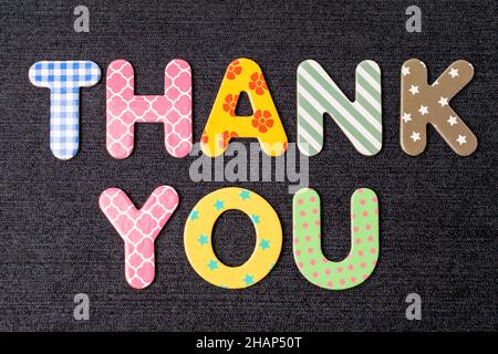 Card with Thank You words made from mixed vivid colored wooden letters on a textured dark black textile material that can be used as a message Stock Photo