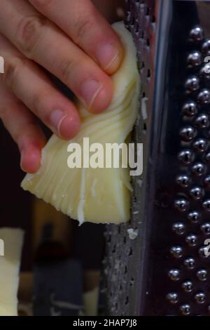 Close up of woman's hand grating cheese on the metal grater Stock Photo