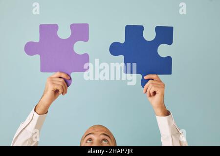 Man holding and connecting purple and blue jigsaw puzzle pieces that match perfectly Stock Photo