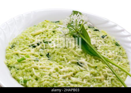 Ramsons (wild garlic leek ) risotto with parmesan cheese, served in a white plate with fresh ramson leaves and flowers as decoration on white backgrou Stock Photo