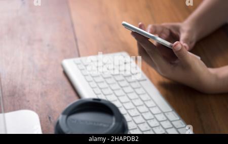 Woman hand using smart phone with computer desktop and coffee cup on wood table Stock Photo