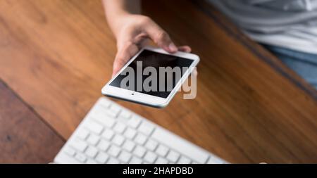 Woman hand using smart phone with computer desktop  on wood table Stock Photo