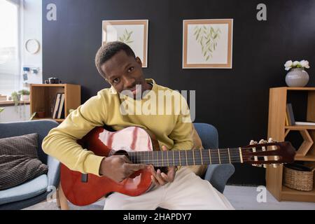 Young smiling African man with acoustic guitar sitting in front of camera and looking at you against home environment Stock Photo